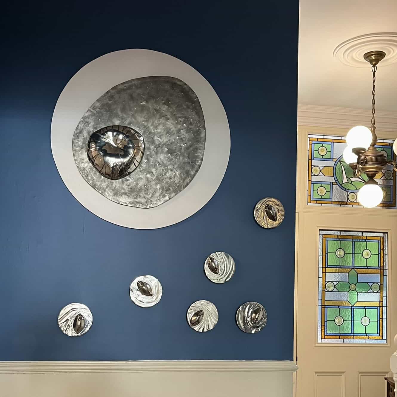 pewter whirligig beetle on disc of pewter that is rippled to look like water on a blue wall